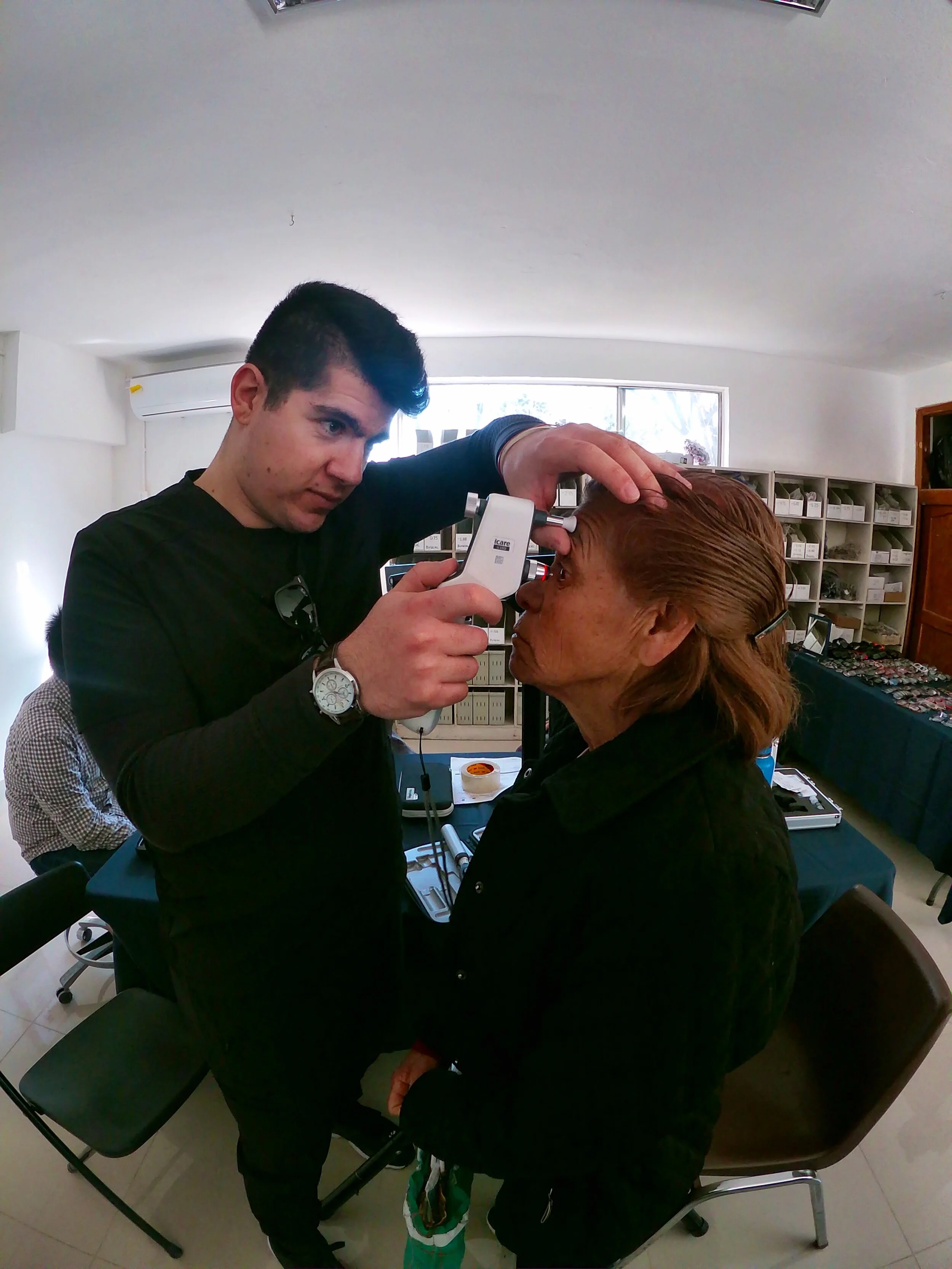 A volunteer examining a patient's eyes with a handheld instrument at the Tecate clinic