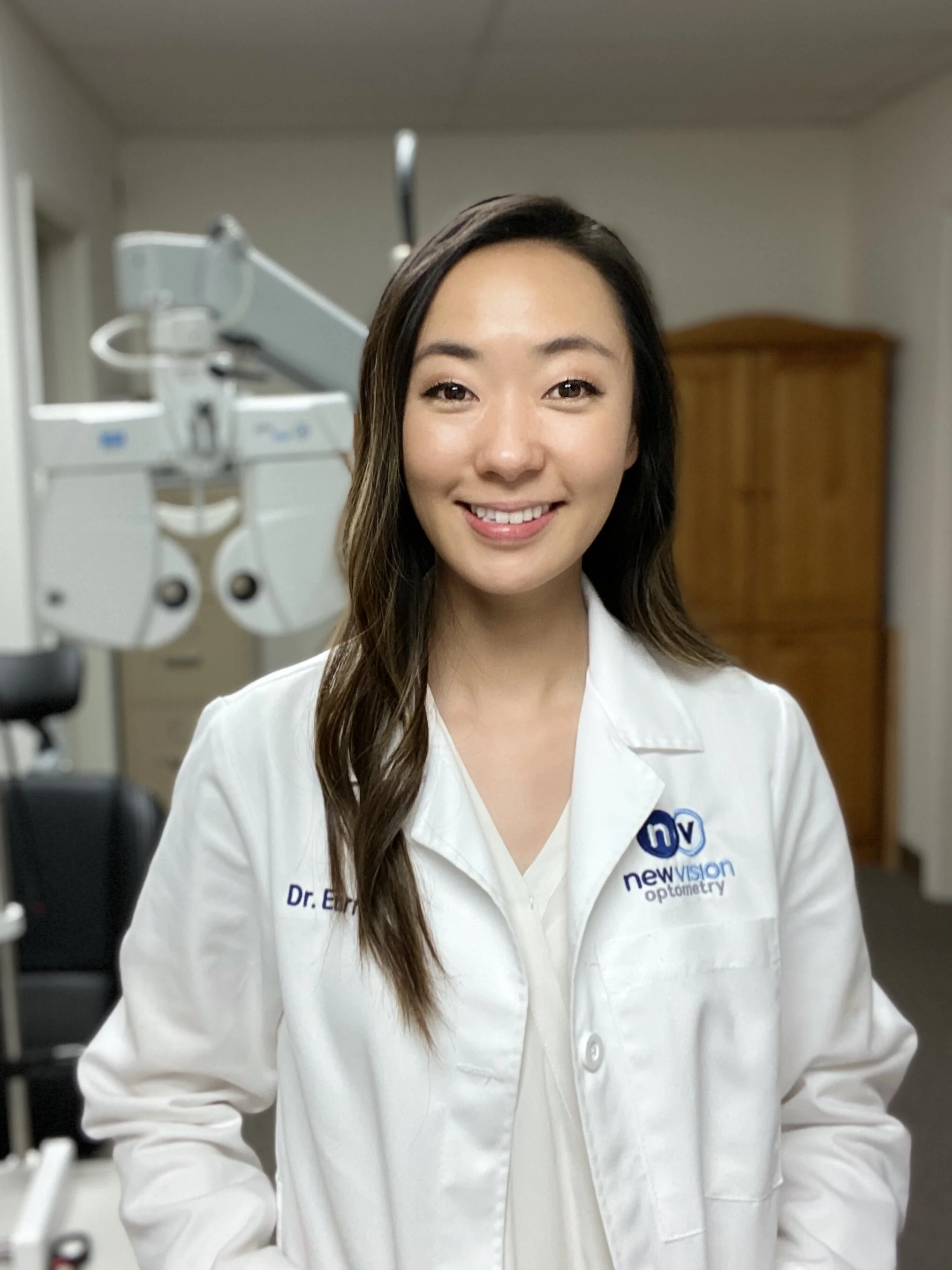 Portrait of Dr. Eurri Choi, O.D., wearing a white coat with the New Vision Optometry logo
