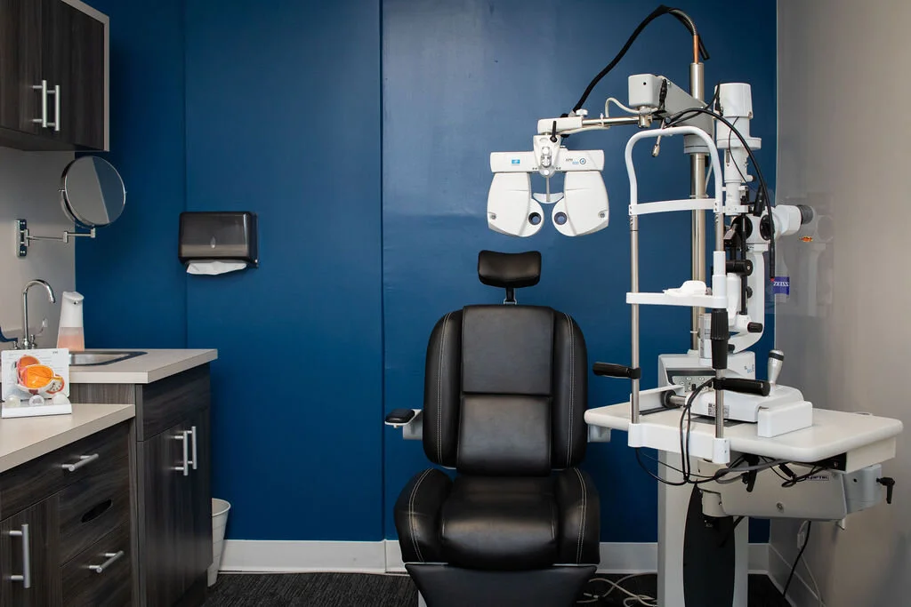 An examination lane at New Vision Optometry, a patient chair and phoropter set against a deep cobalt wall