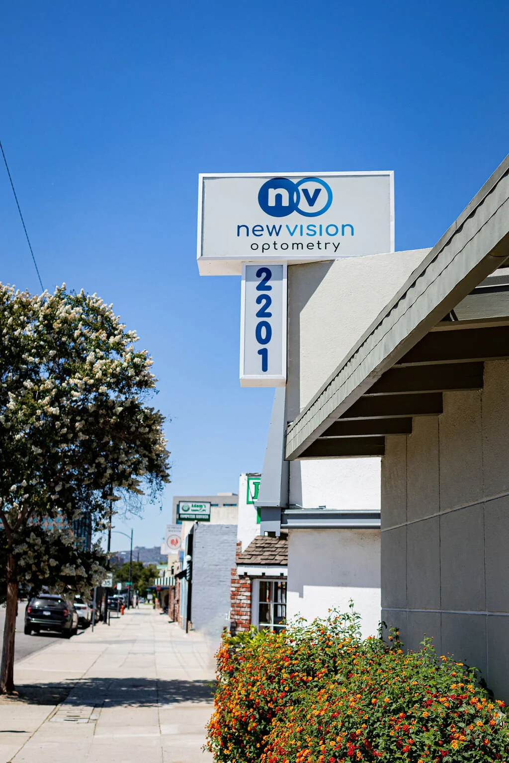 The New Vision Optometry street sign outside 2201 West Olive Avenue, the practice monogram above the street number