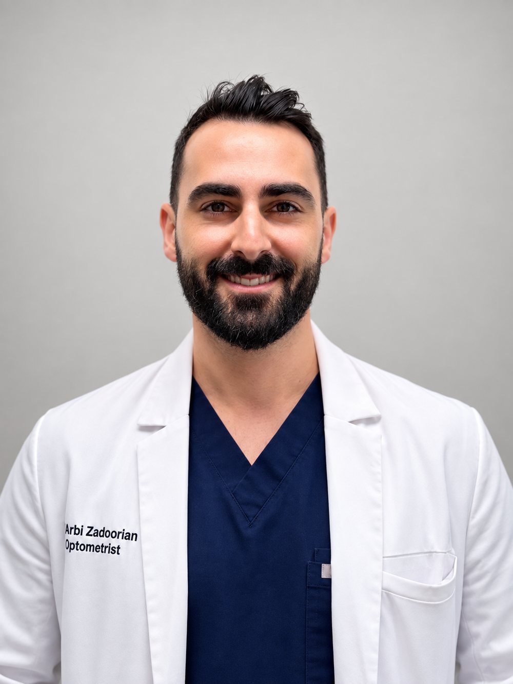 Portrait of Dr. Arbi Zadoorian, O.D., in a white coat over navy scrubs, photographed in September 2026