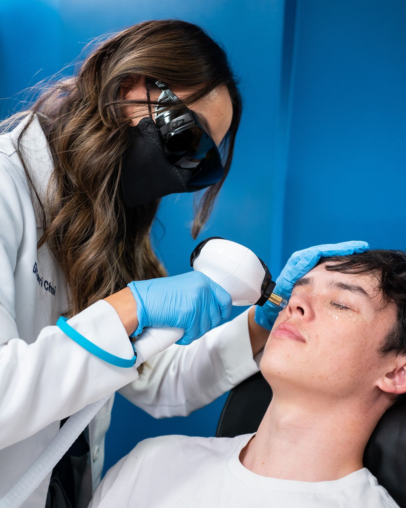 Dr. Choi in a white coat and protective goggles giving an IPL treatment to a reclined patient at New Vision Optometry