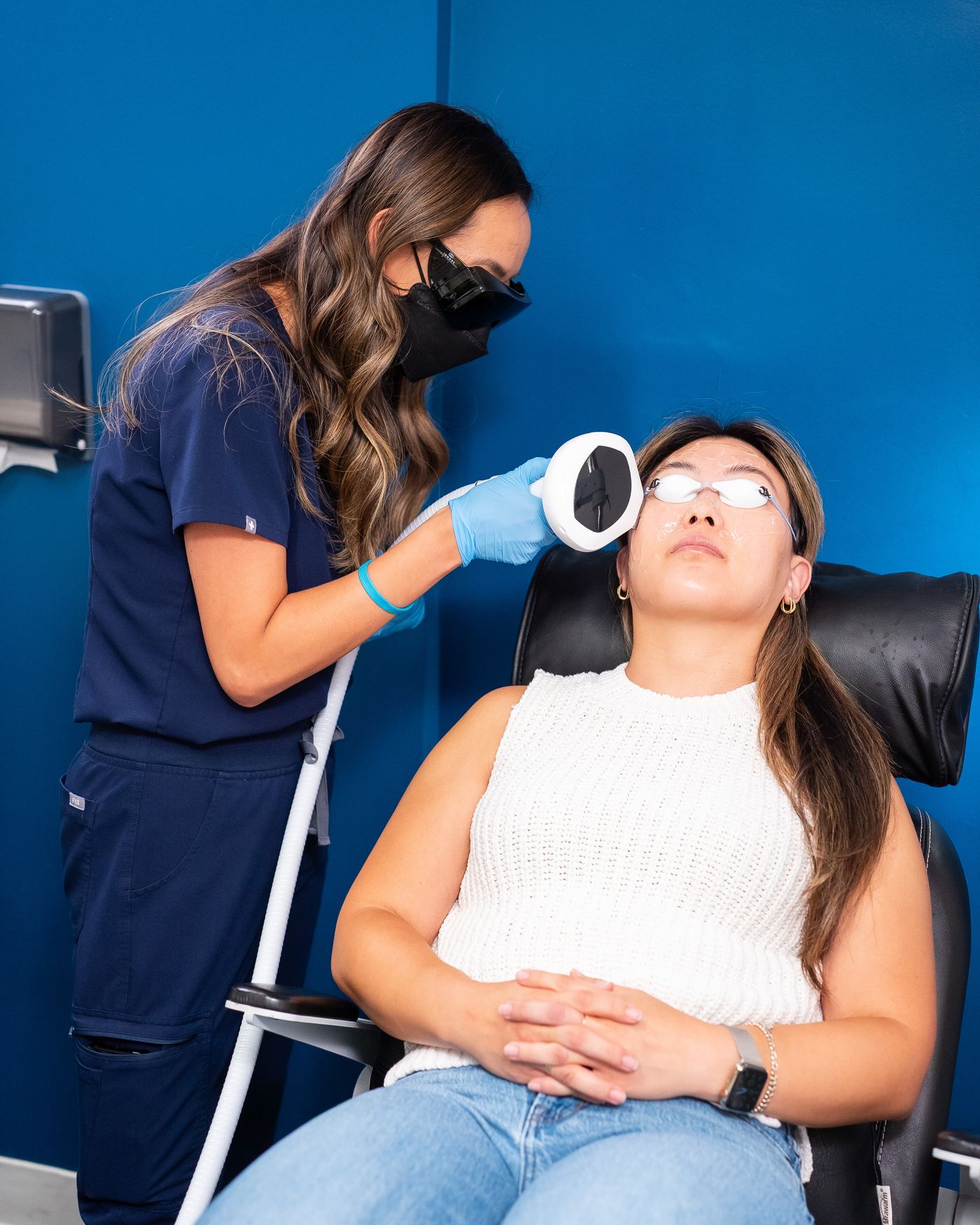 An IPL treatment in progress at New Vision Optometry, the patient reclined in protective goggles while the Lumecca handpiece is held to her cheek