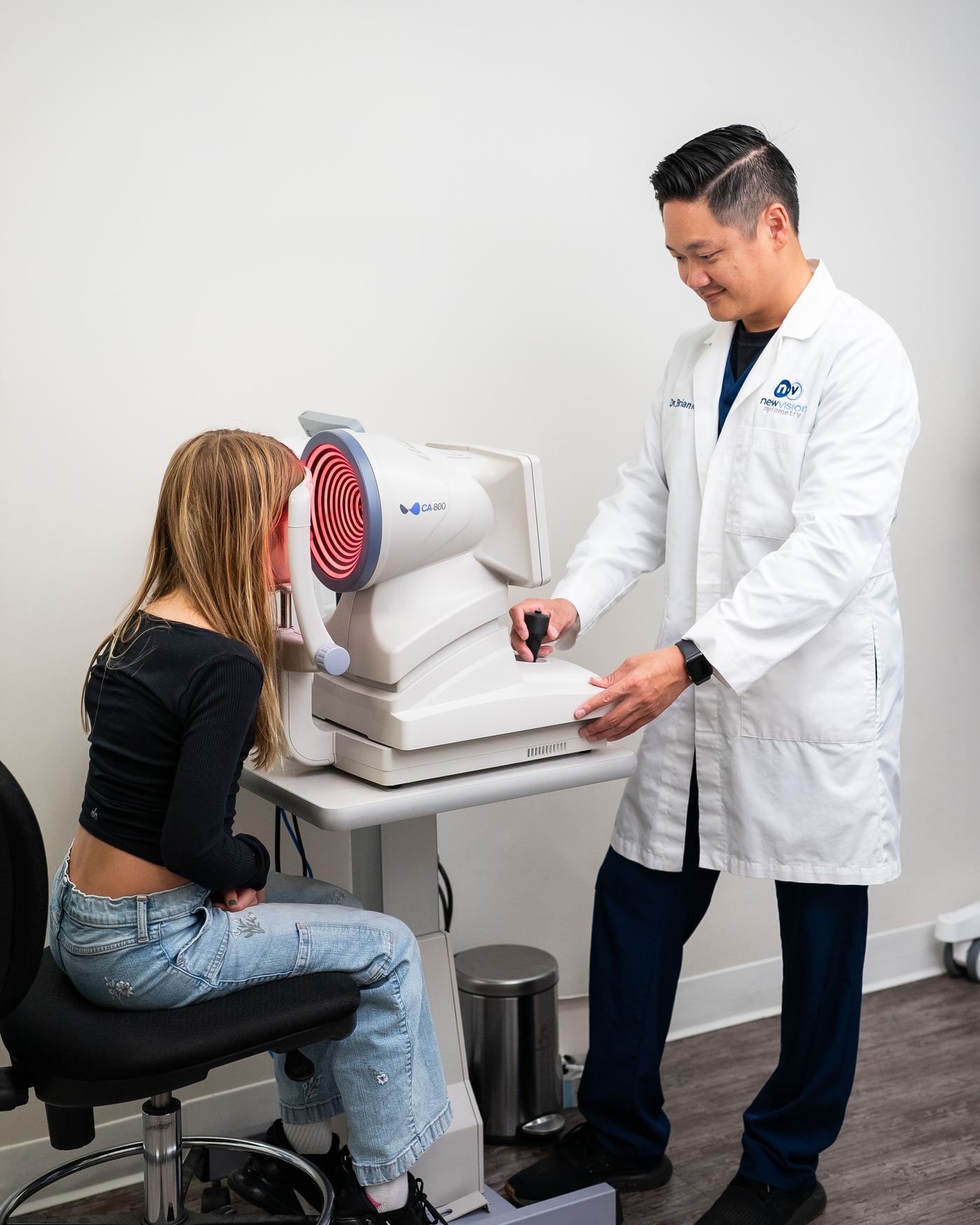 Dr. Nguyen beside a young patient seated at the corneal imaging instrument in the testing area at New Vision Optometry