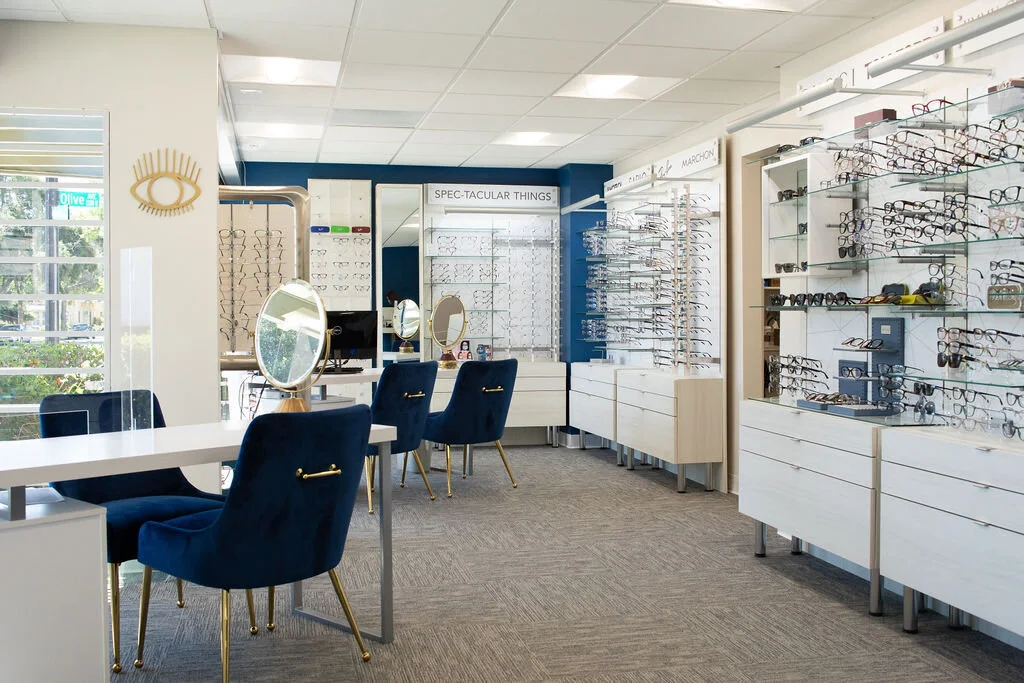 The optical at New Vision Optometry, frames along a bright wall with navy velvet chairs and brass fittings