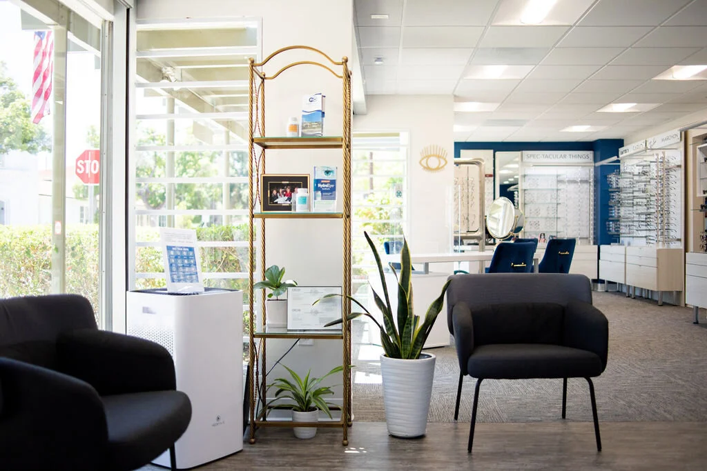 The front of New Vision Optometry, dark armchairs and a brass etagere beside the daylight windows, with the optical and its frame displays behind